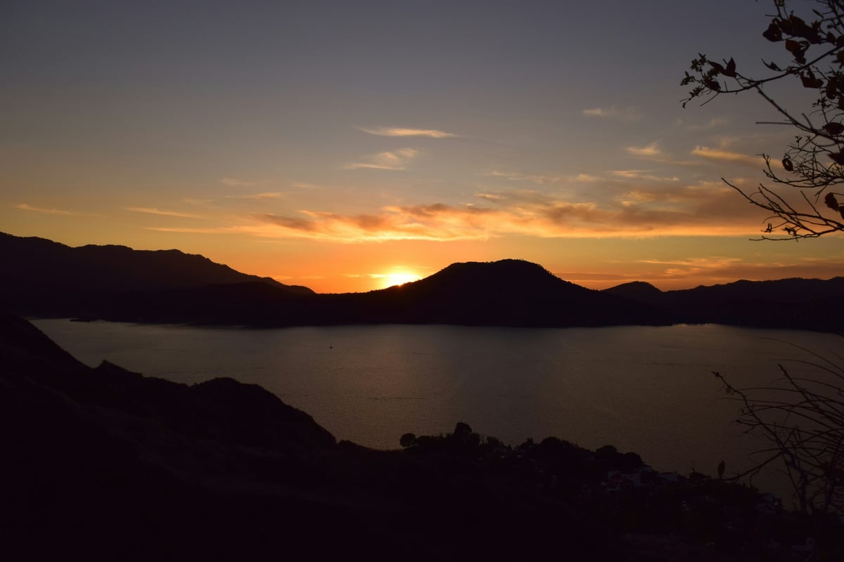 Atardecer anaranjado sobre un lago rodeado de montañas en silueta